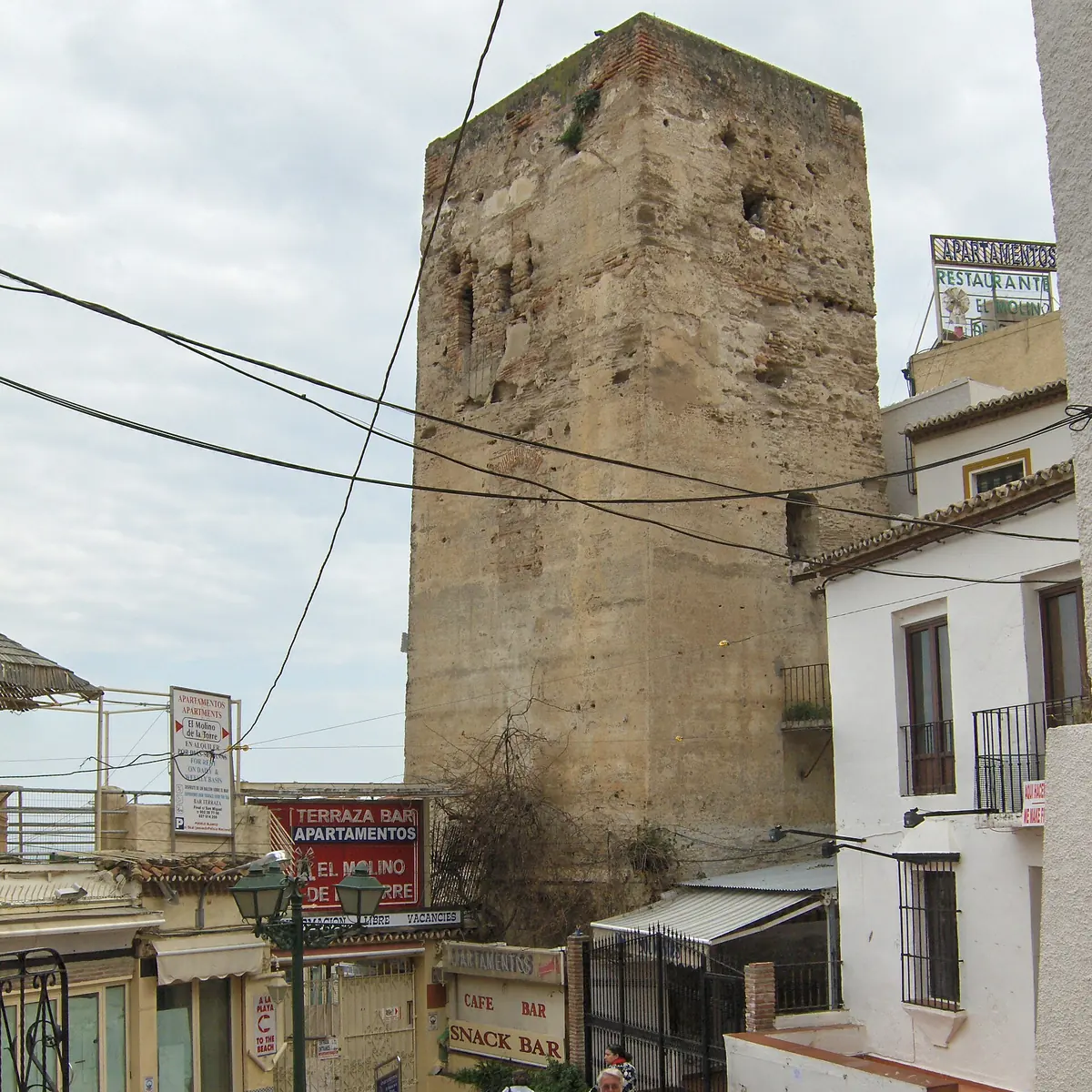 The square stone tower in Torremolinos rising above whitewashed houses and a narrow street with shop signs